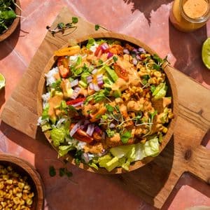 Overhead view of a vegan cauliflower taco salad topped with taco-seasoned cauliflower and lentils, cilantro lime rice, romaine lettuce, fire-roasted corn, avocado, cherry tomatoes, red onion, microgreens, and creamy chipotle ranch dressing in a wooden bowl.