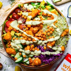 Close-up of vegan buffalo cauliflower salad with crispy chickpeas, avocado, cucumber, cherry tomatoes, sprouts, purple cabbage, and creamy dairy-free ranch dressing