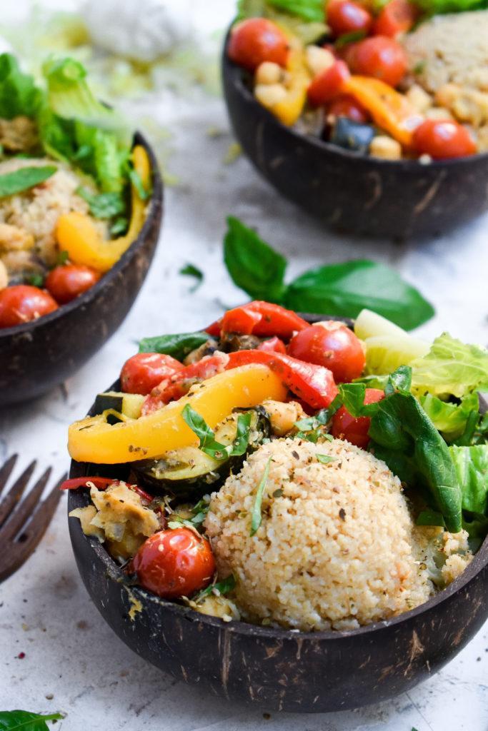 Mediterranean stir fry served over couscous and romaine lettuce in a coconut bowl