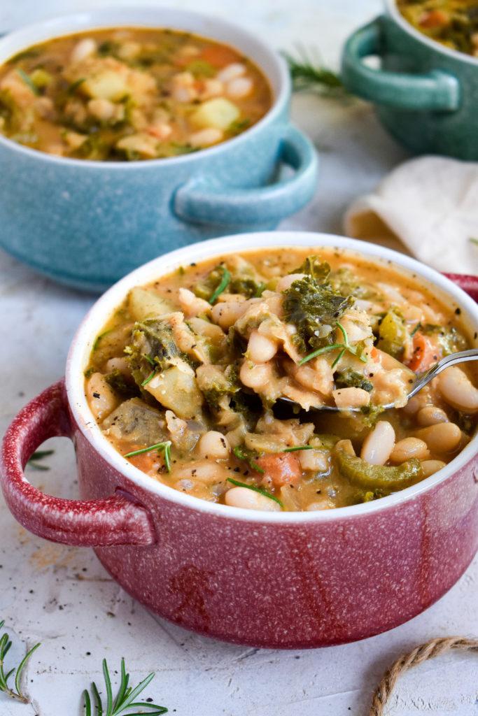 vegan white bean soup with a spoon cooping up the creamy white beans and kale
