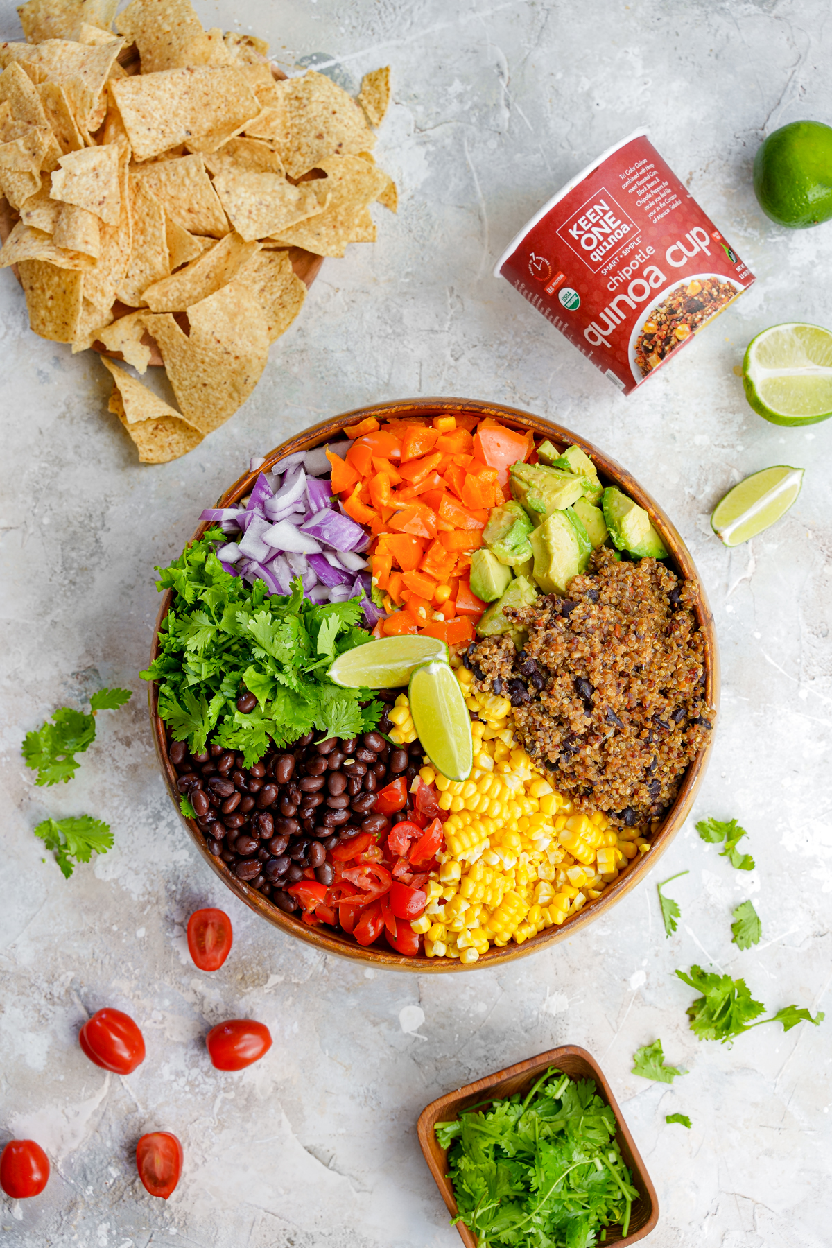 giant bowl of quinoa cowboy caviar pre mixed with chips and limes to the side and the keen one cups.