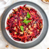 raw vegan beet salad with carrots, walnuts, and raisins, topped with a bit of fresh parsley
