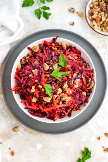raw vegan beet salad with carrots, walnuts, and raisins, topped with a bit of fresh parsley
