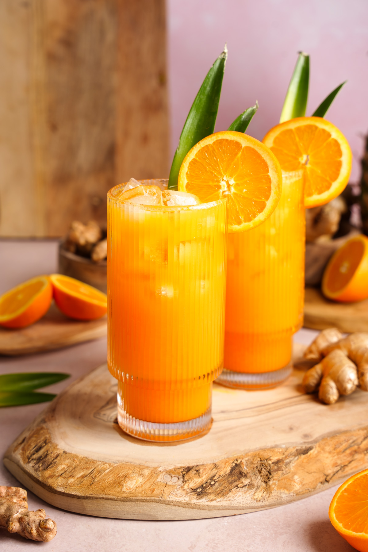 two glasses of the turmeric ginger glow juice garnished with orange slices and pineapple leaves