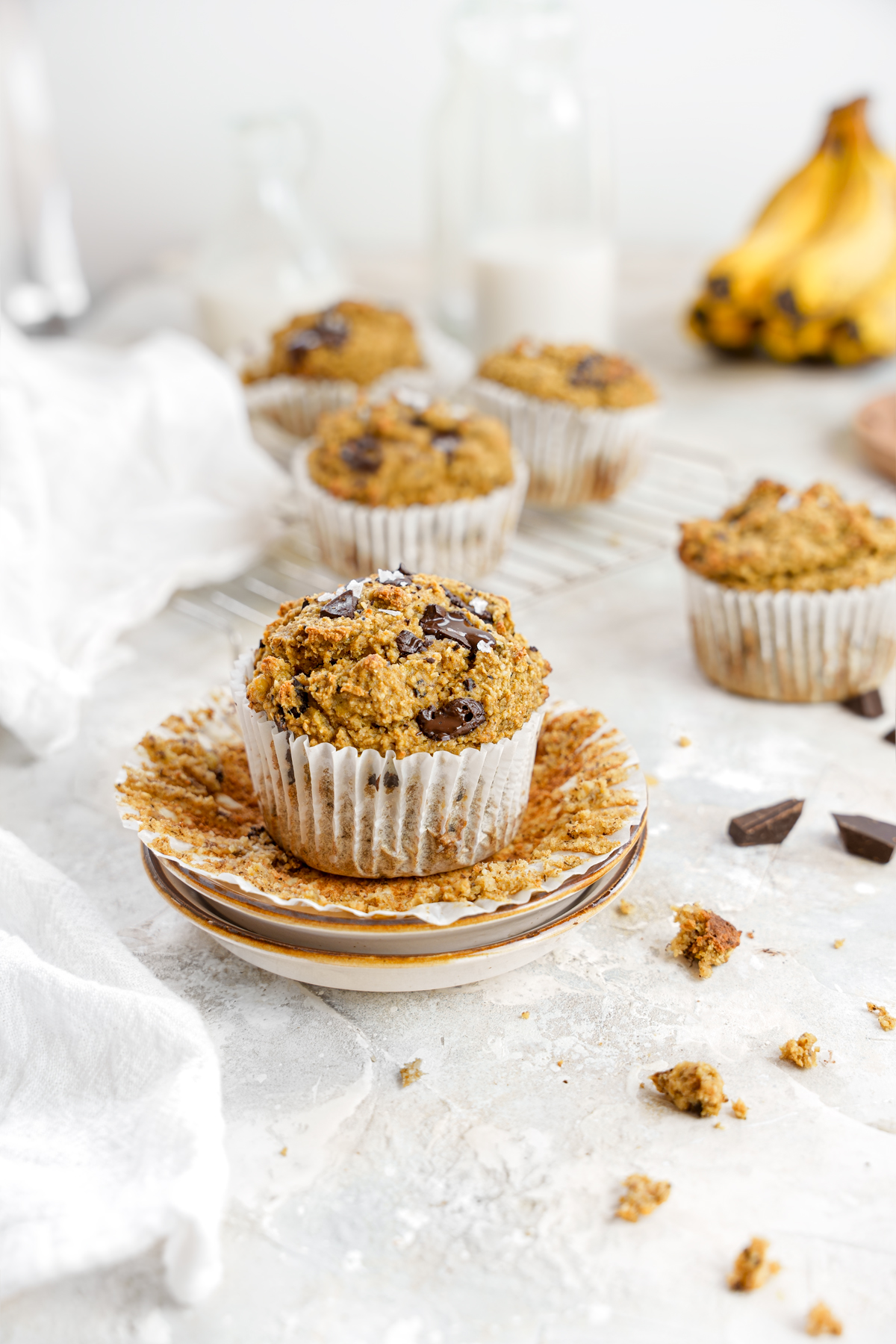 the vegan chocolate chip banana muffins lined up with crumbs and chocolate surrounding them