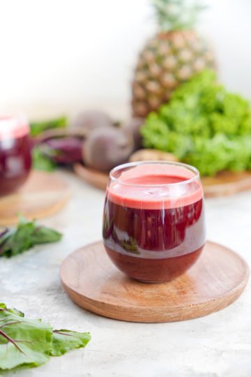 kale beet juice in a cup with pineapple and kale in the background