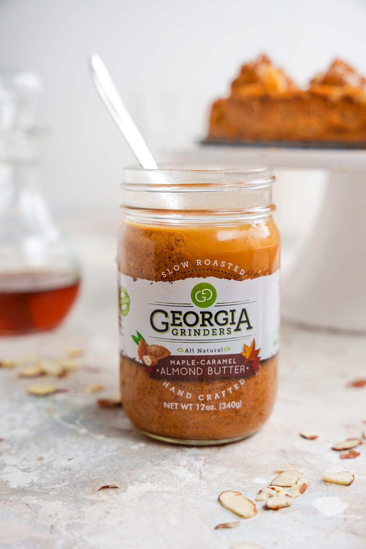 A jar of Georgia grinders maple caramel almond butter with the cheesecake and maple syrup in the background