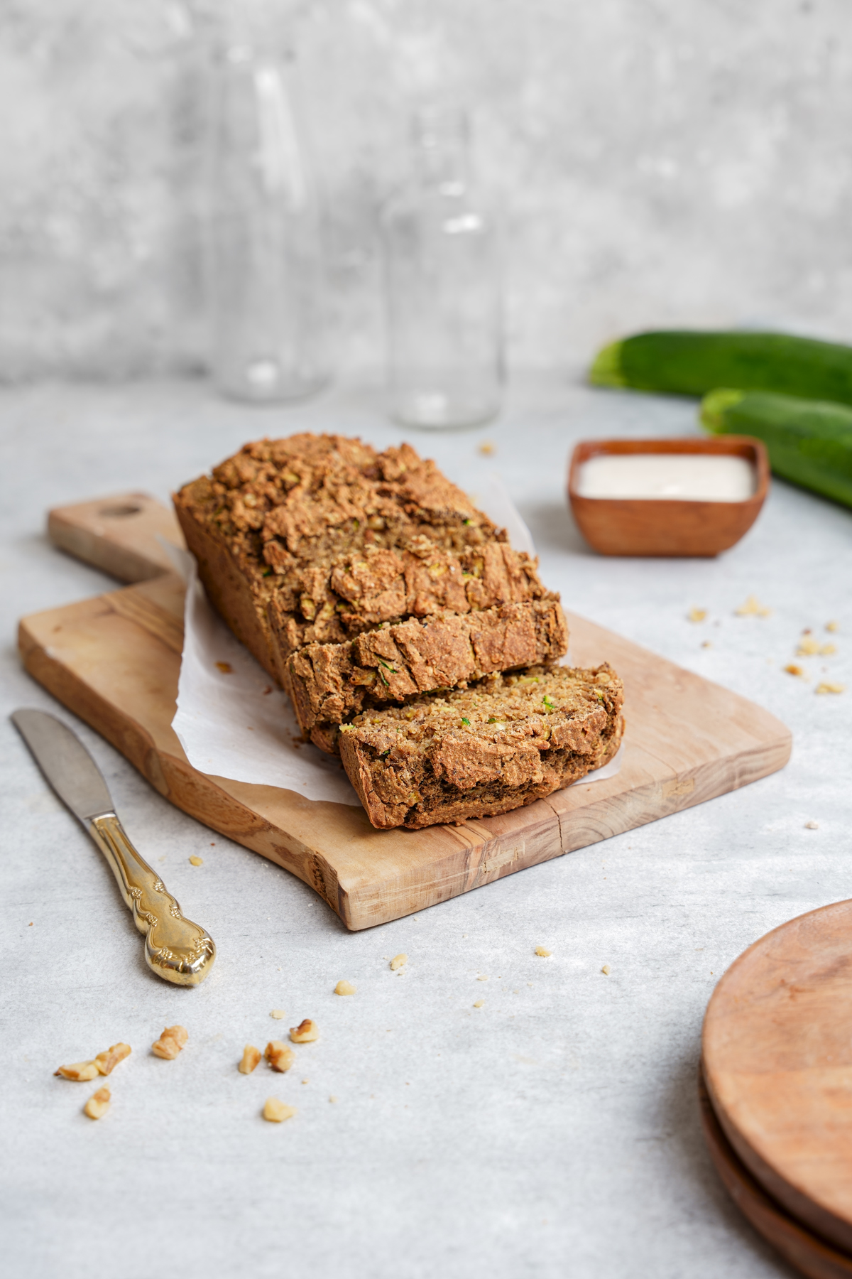 healthy vegan zucchini bread on a cutting board with zucchini in the back