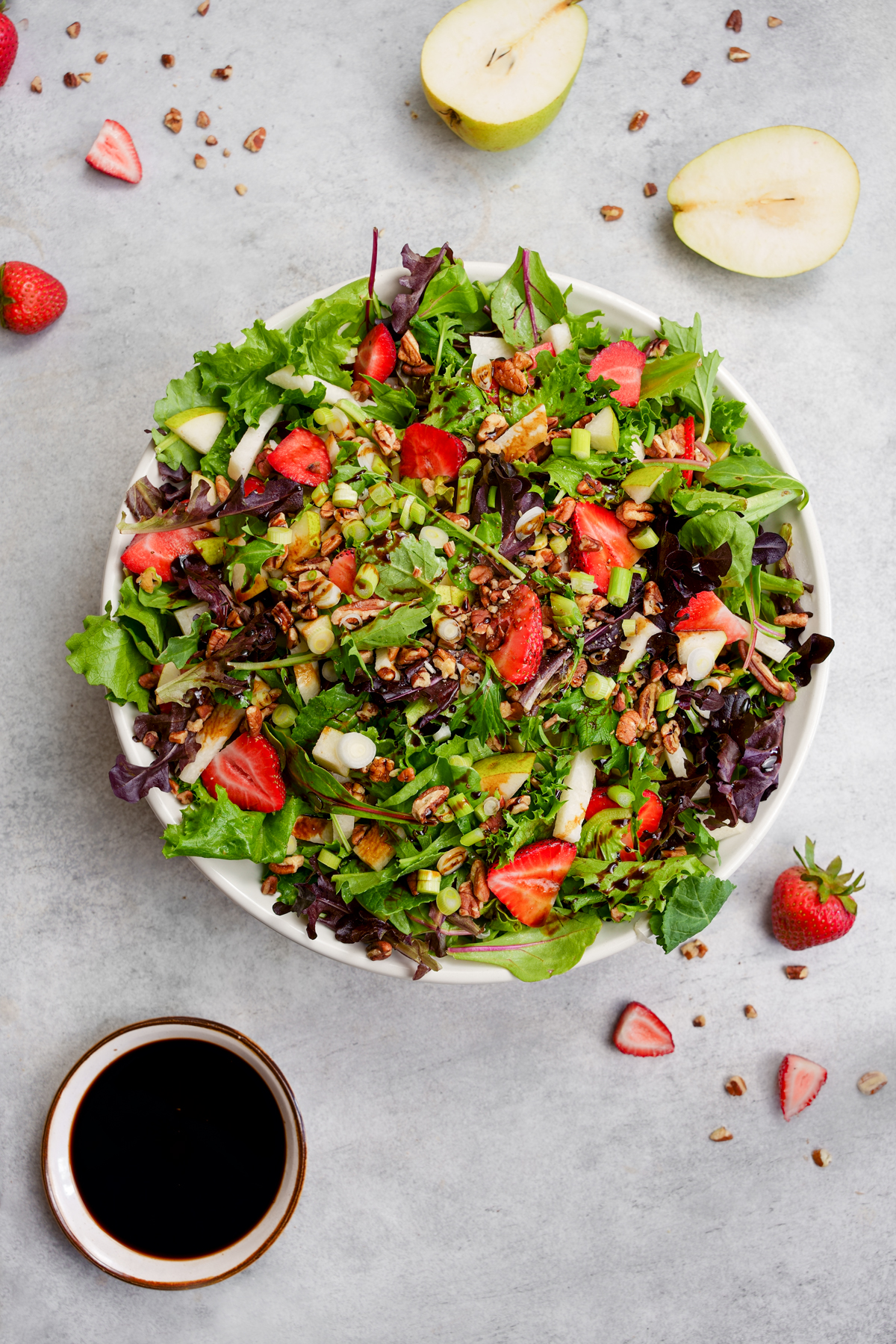large bowl full of the jicama strawberry salad that features strawberries, pears, pecans, spring mix, and jicama