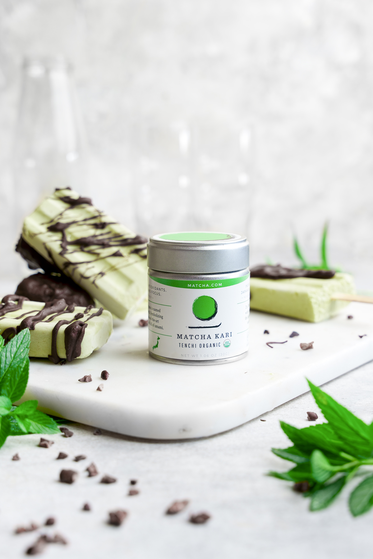 a container of the tenchi organic matcha  with fresh mint leaves and cacao nibs around it