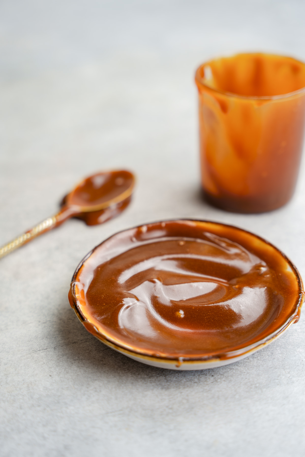 the 2 ingredient vegan date syrup caramel spread on a plate with a caramel covered spoon