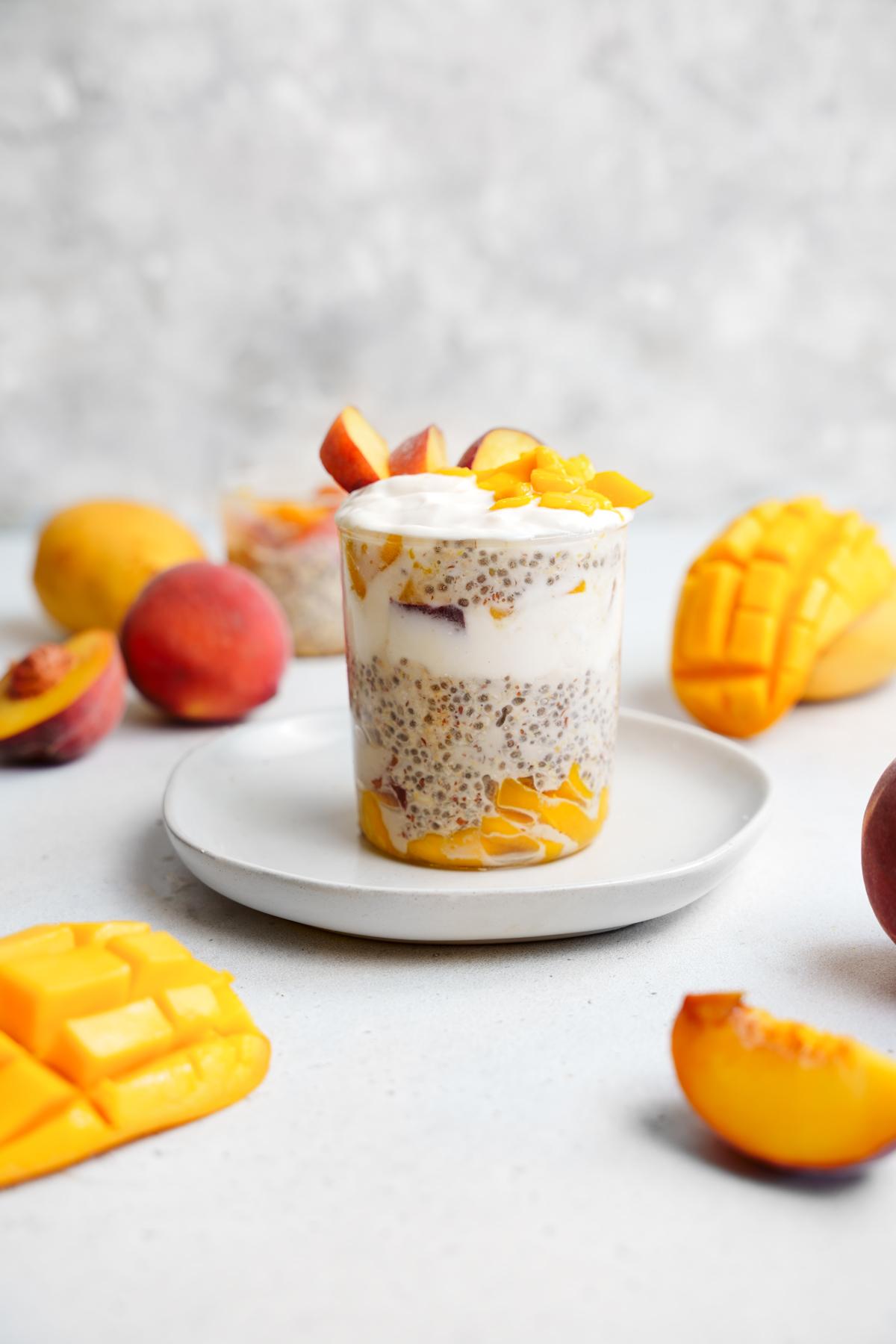 the mango oatmeal with layers of fresh peaches and mango, coconut yogurt, and oats surrounded by fresh cut peaches and mango