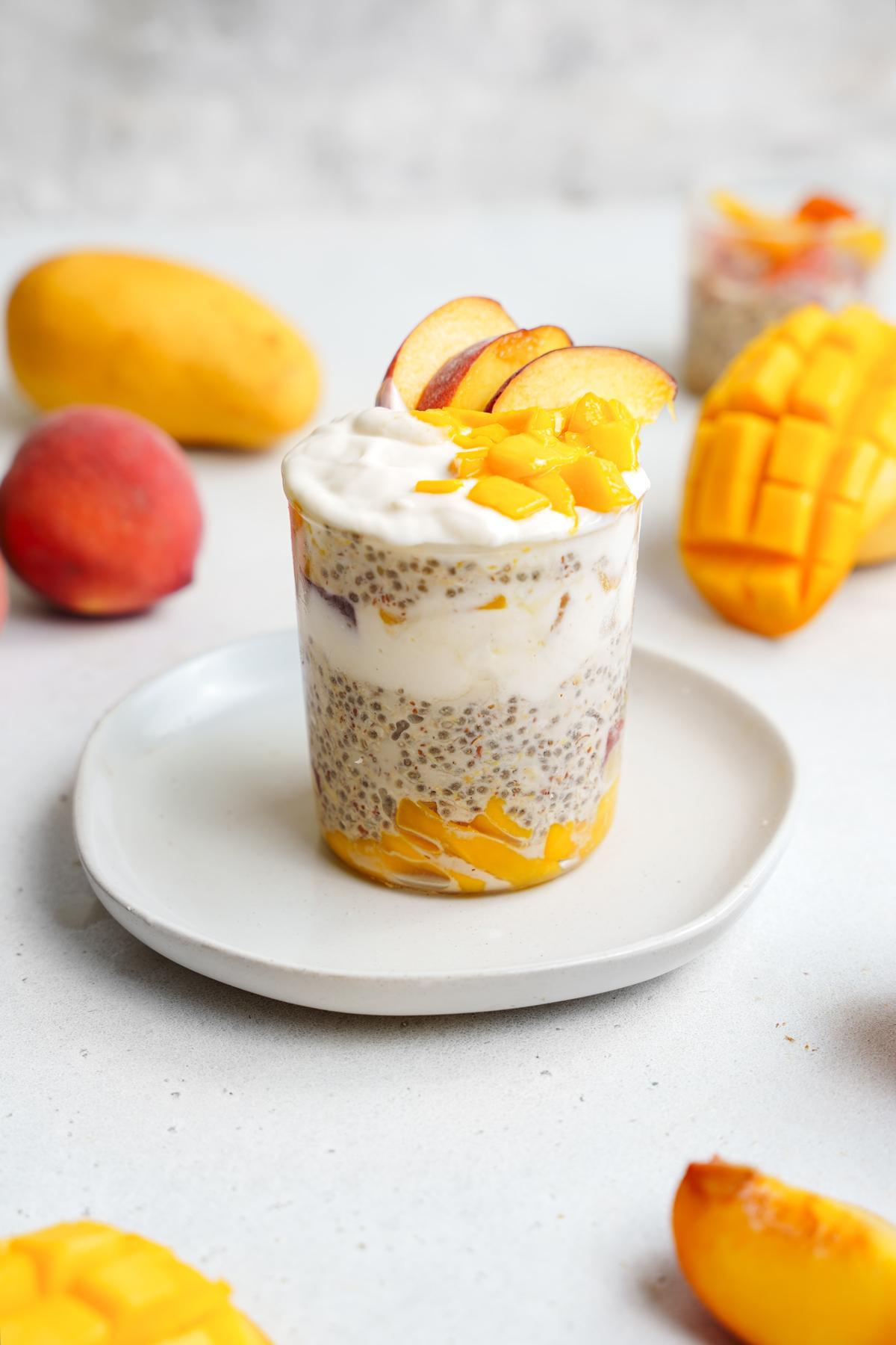 the mango overnight oats in a glass cup with coconut yogurt and fresh peaches and mango on top