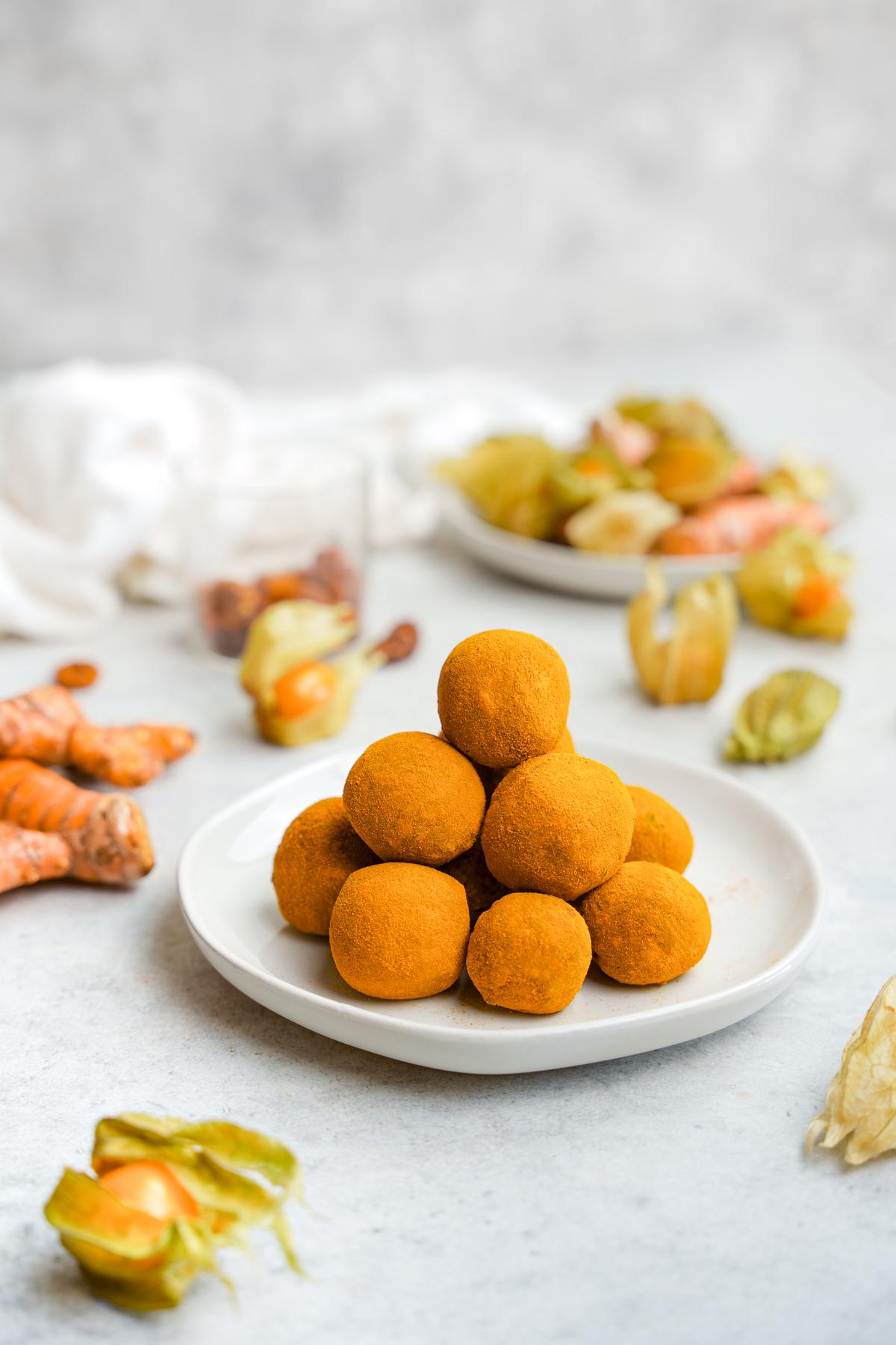 the perfect circle turmeric balls stacked on a plate surrounded by fresh turmeric root and golden berries