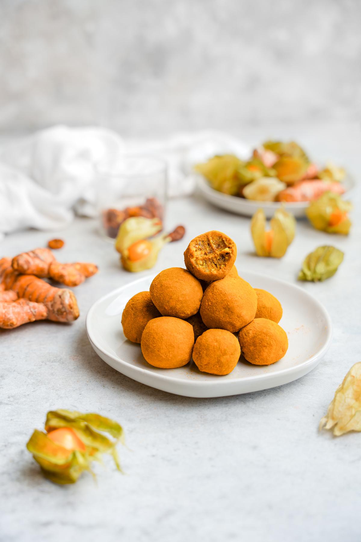 the turmeric balls stacked on top of each other with one that has a bite taken out of it. The balls are surrounded by fresh turmeric and golden berries