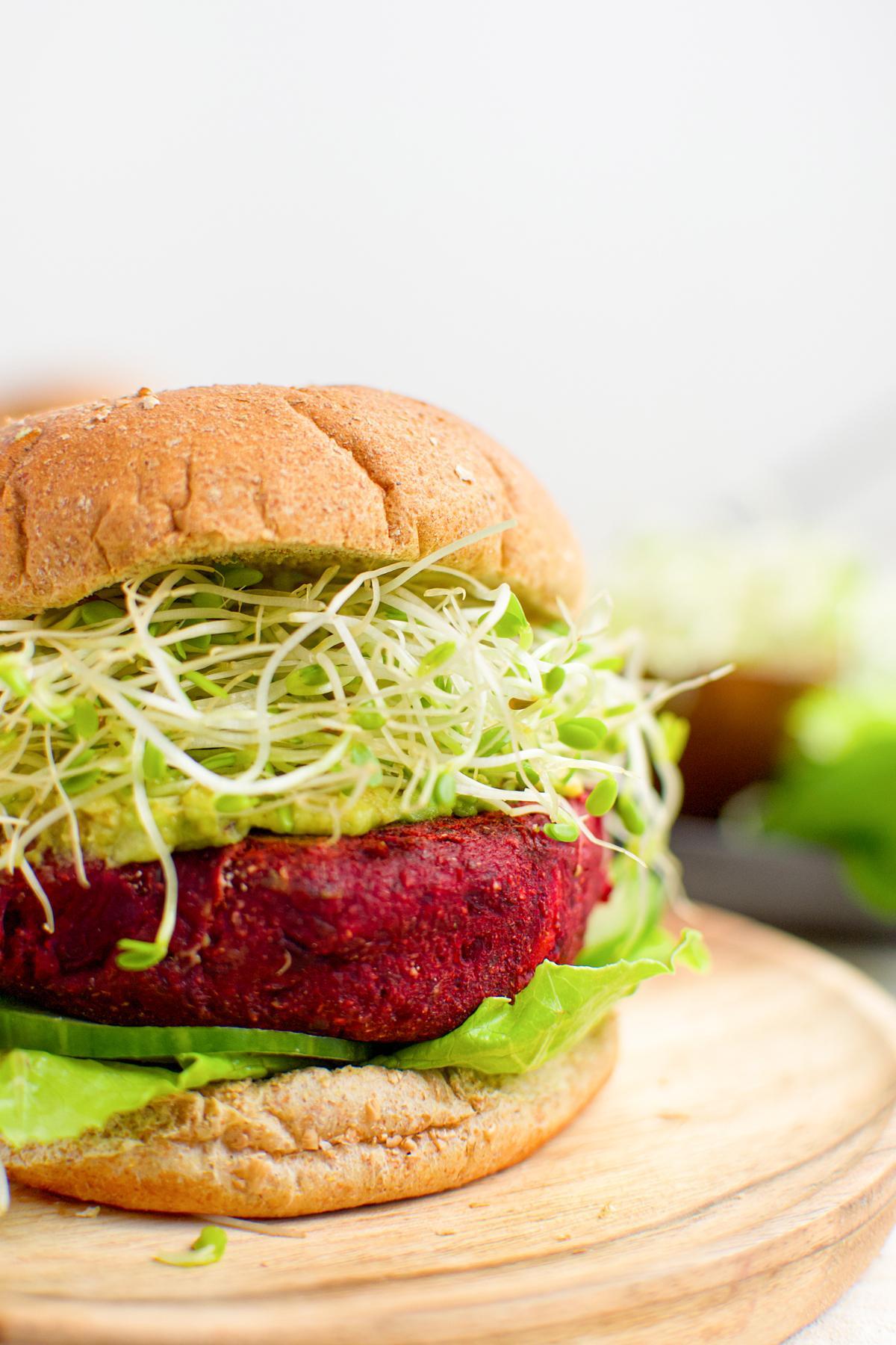 close up of the sweet potato beet burger with sprouts, mashed avocado, and cucumber, on gluten-free buns to show the tender and moist patty