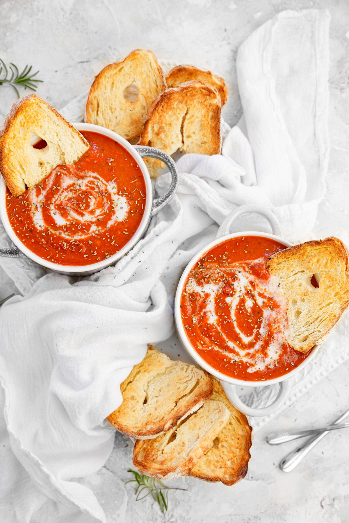 two bowls of the whole foods plant based tomato soup with bread and herbs on top