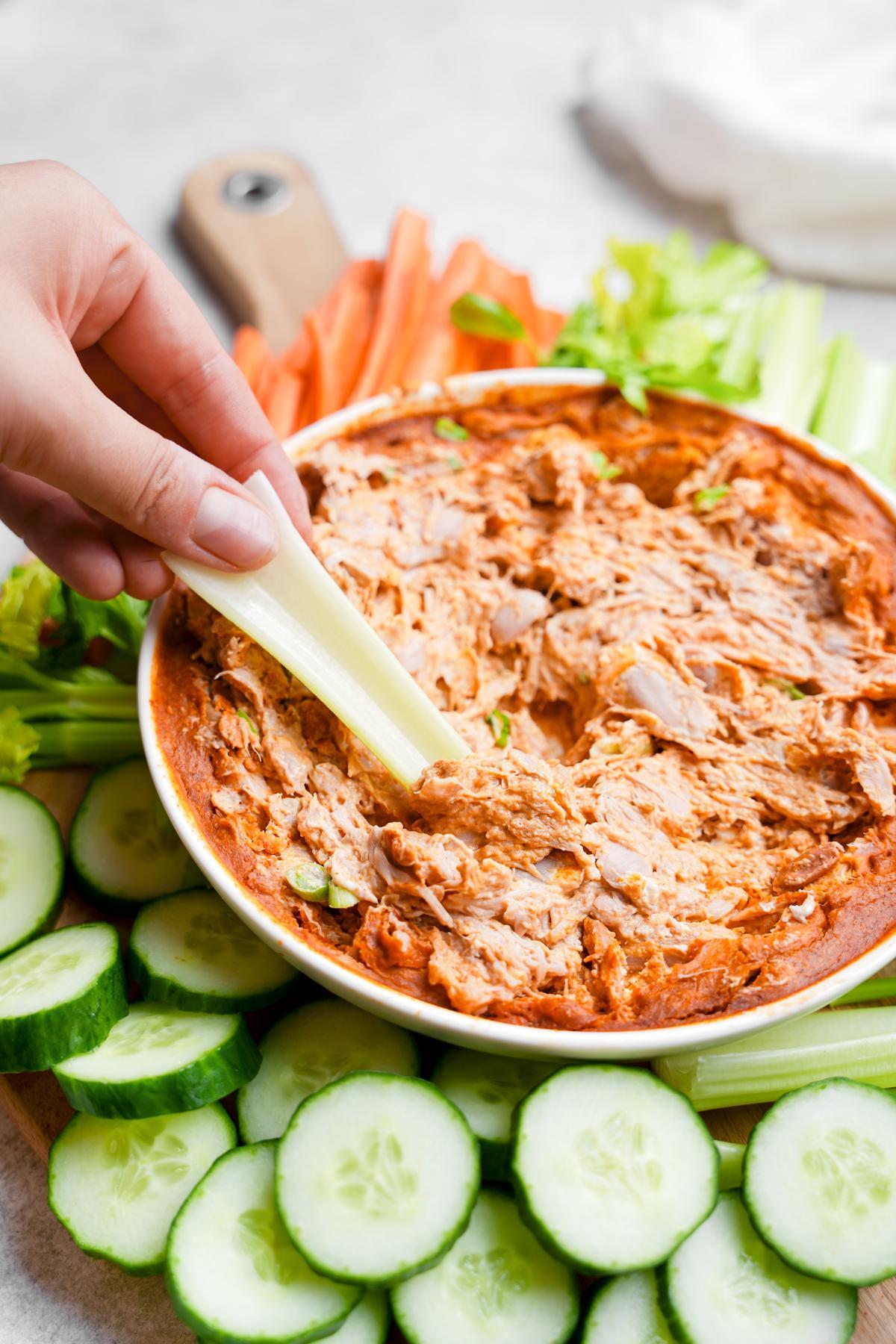 the vegan buffalo chicken dip with a hand dipping celery into it