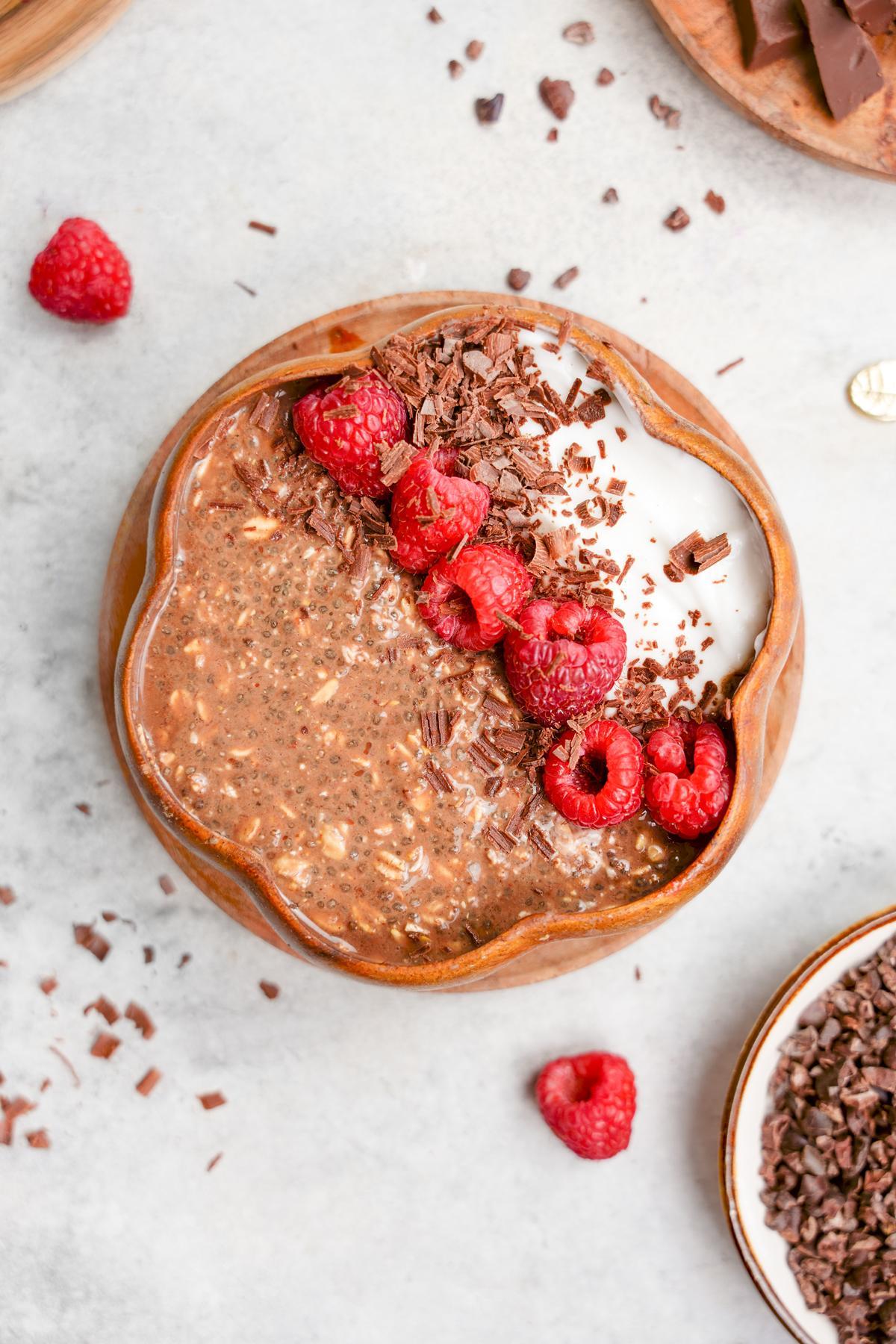 the chocolate raspberry overnight oats topped with fresh raspberries, dark chocolate, and vegan yogurt