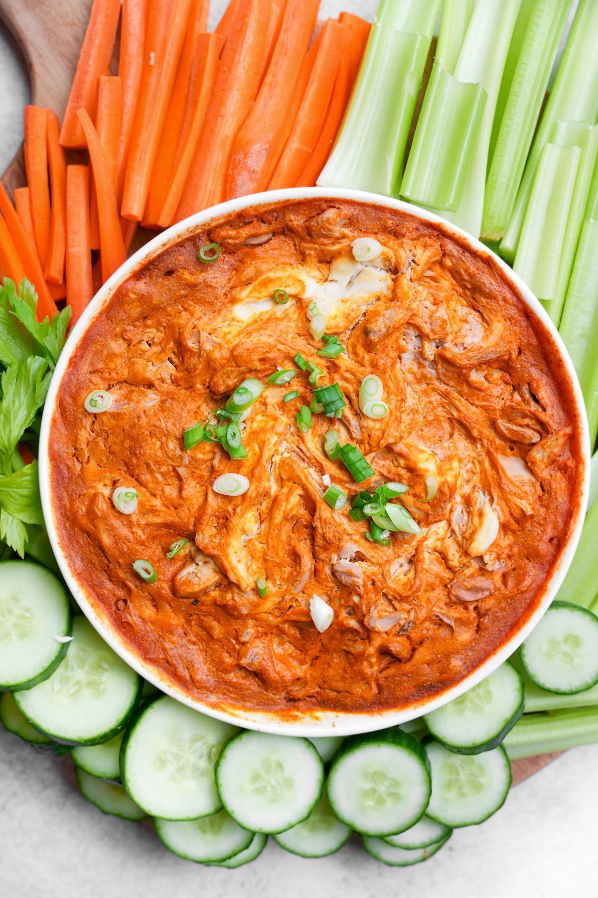 close up of the jackfruit buffalo dip with green onions on top and fresh vegetables for dipping