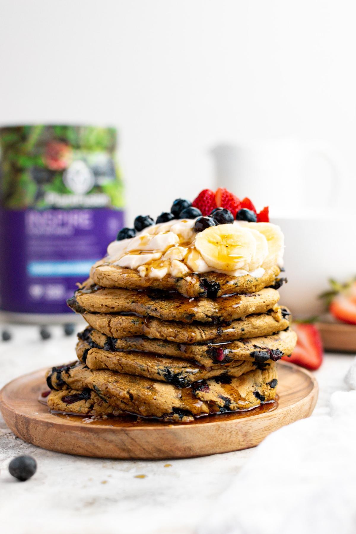 the oatmeal blueberry protein pancakes stacked on top of each other with maple syrup poured over them