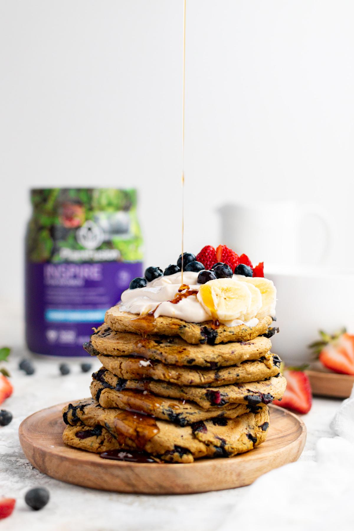 pouring the maple syrup over the vegan blueberry protein pancakes