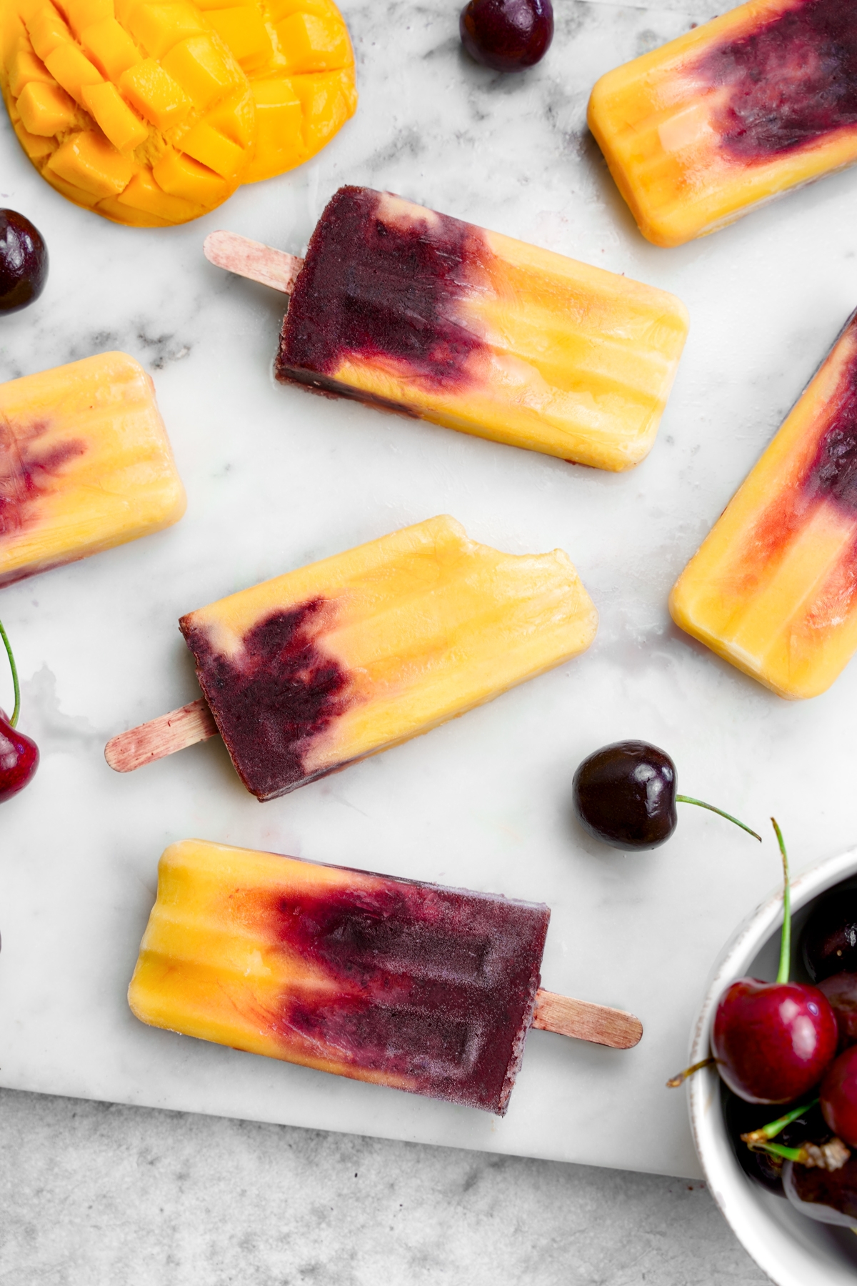 the mango cherry popsicles laying flat with a bite taken out of one