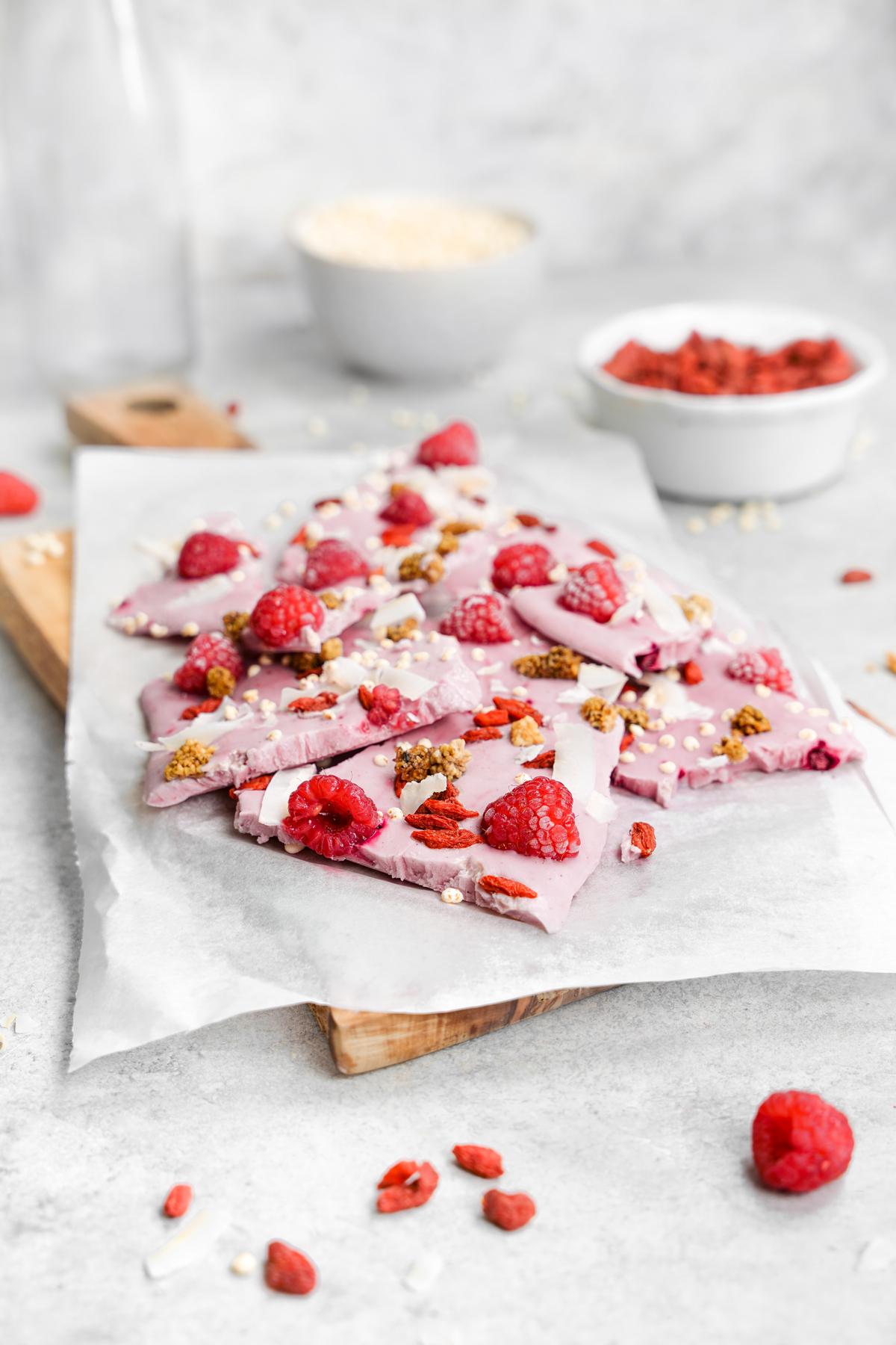 the superfood vegan yogurt bark stacked on top of each other with raspberries, mulberries, goji berries, and coconut on top