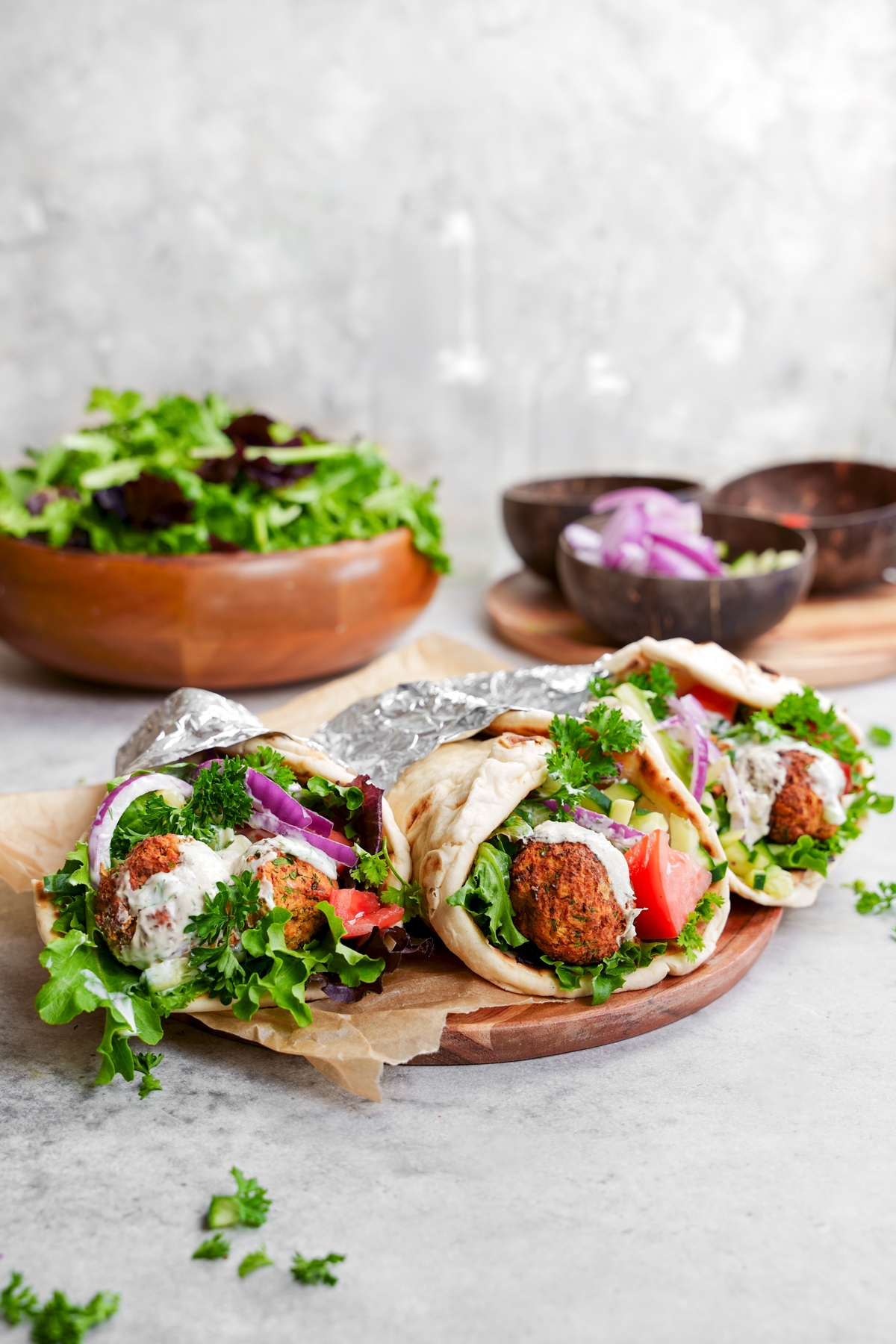 falafel gyros wrapped in foil on a plate with fresh greens and dairy-free tzatziki sauce