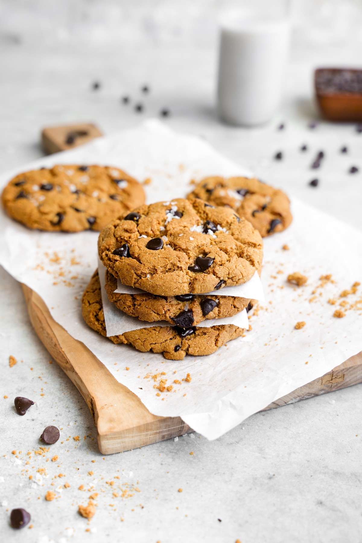healthy vegan chocolate chip cookies stacked on top of each other with cookie crumbs and chocolate around them