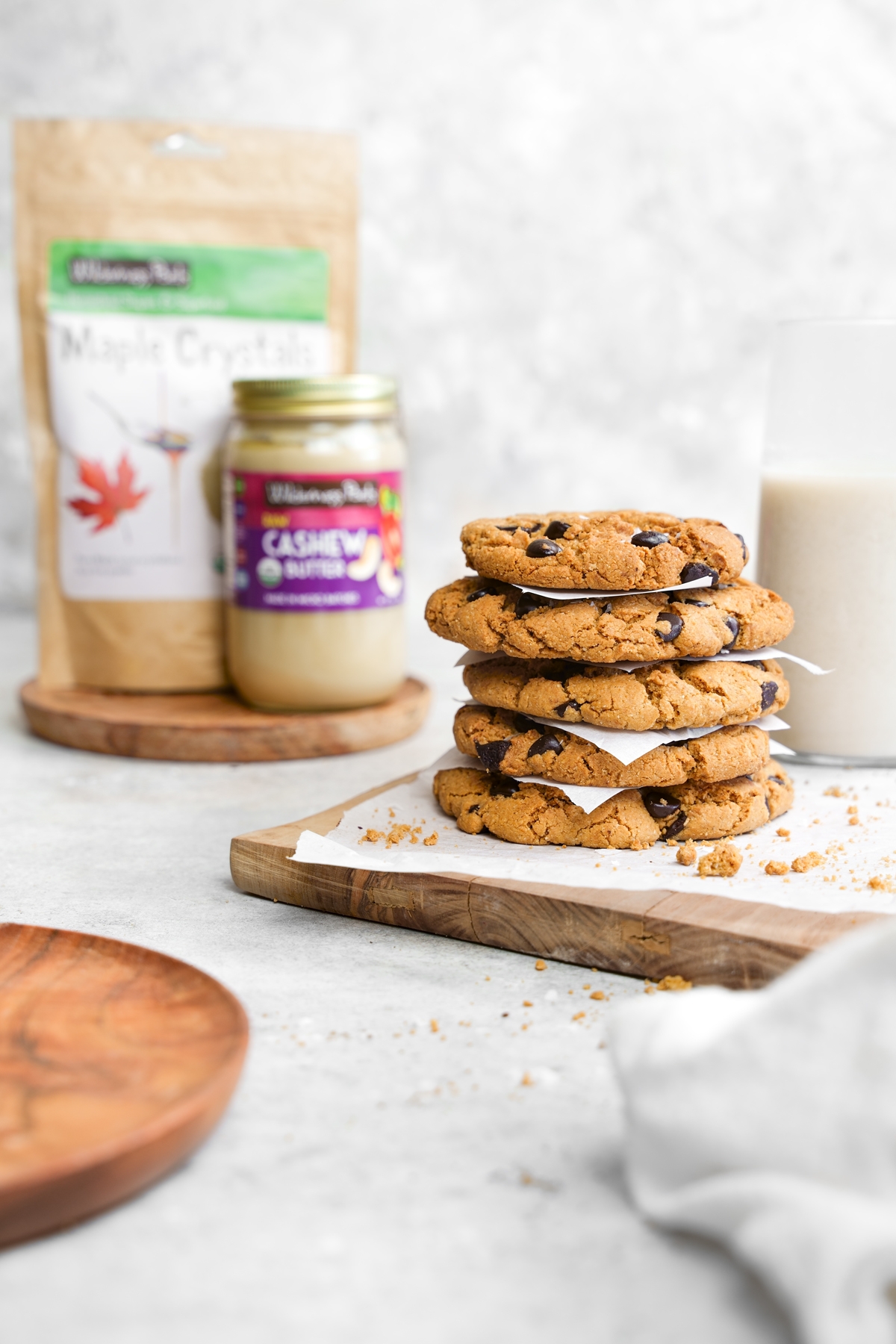 the healthy vegan chocolate chip cookies stacked on top of each other with the raw cashew butter and maple crystals from wilderness poets