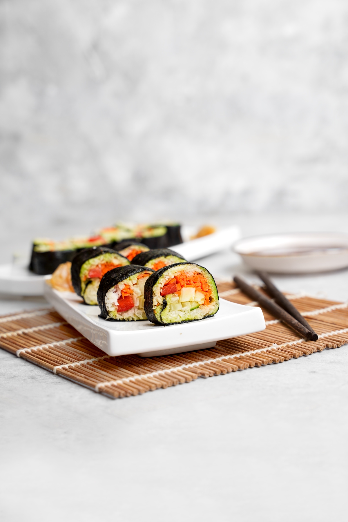 raw vegan sushi cut into slices on a sushi dish with chopsticks