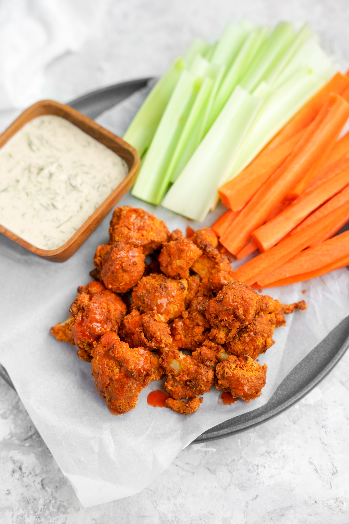 the air fryer buffalo cauliflower bites on a plate with carrots, celery, and homemade vegan ranch dressing.