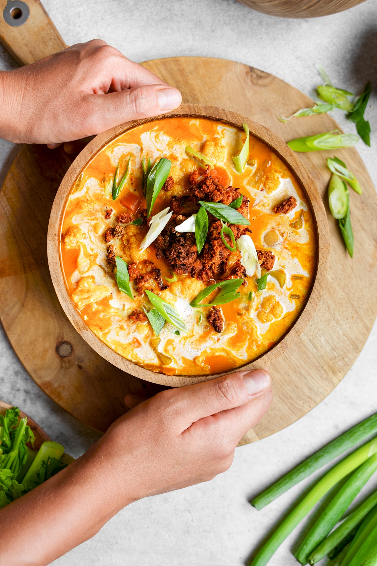 hands holding the buffalo cauliflower soup in a large bowl topped with air fried cauliflower and green onions