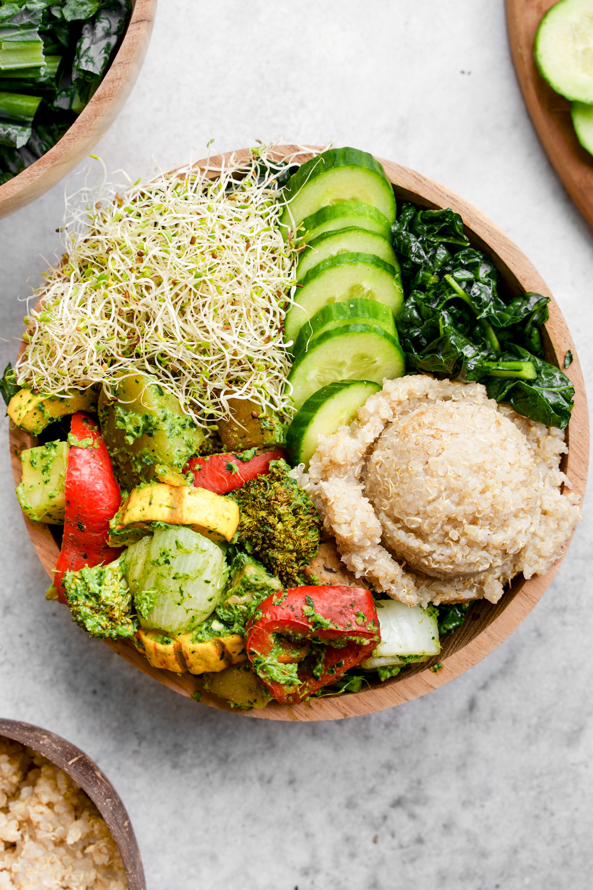 looking down at the pesto buddha bowl made up of roasted vegetables, kale, quinoa, sprouts, and cucumbers