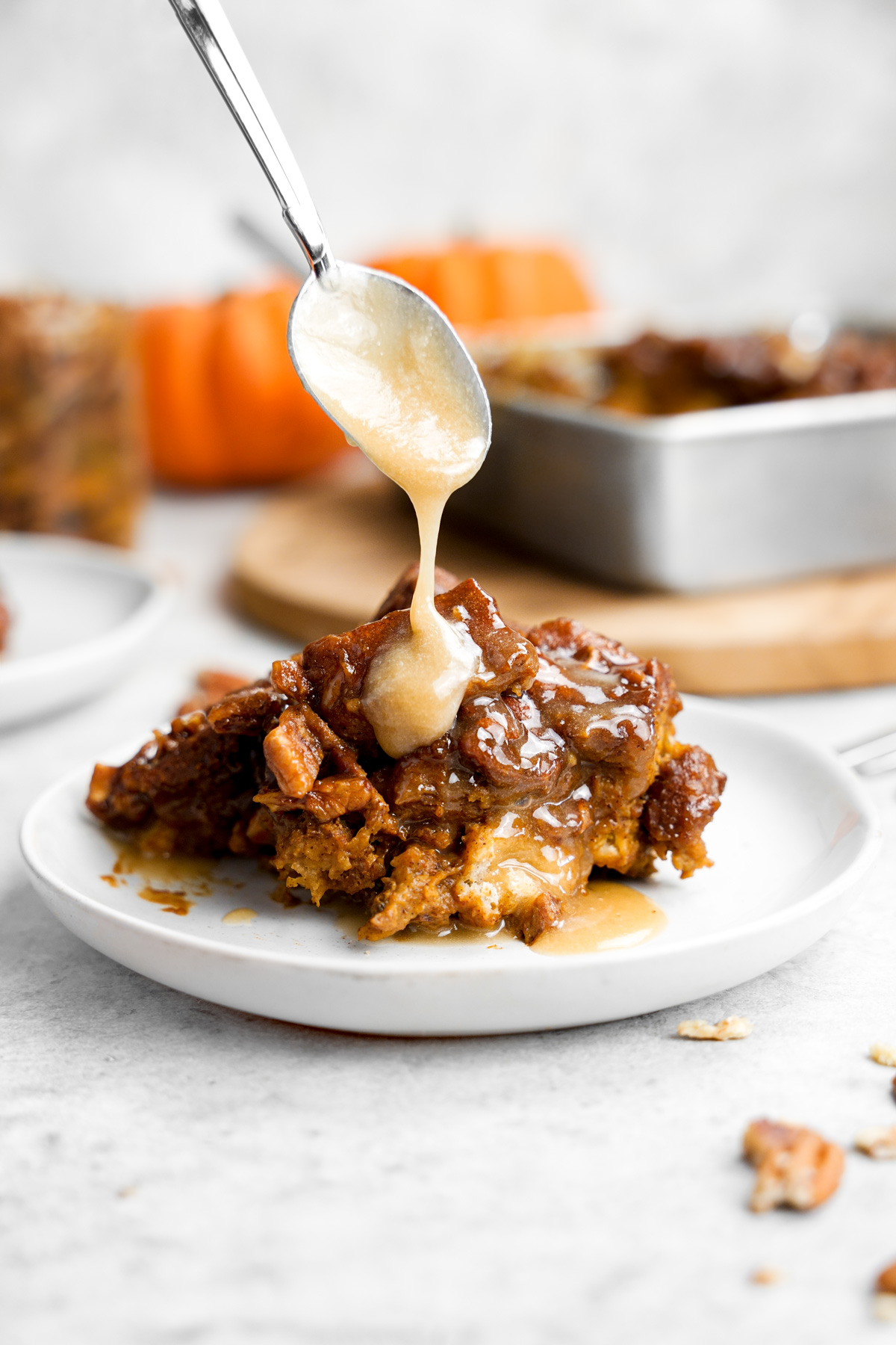 the vegan pumpkin bread pudding with a spoon drizzling the maple cream glaze on top