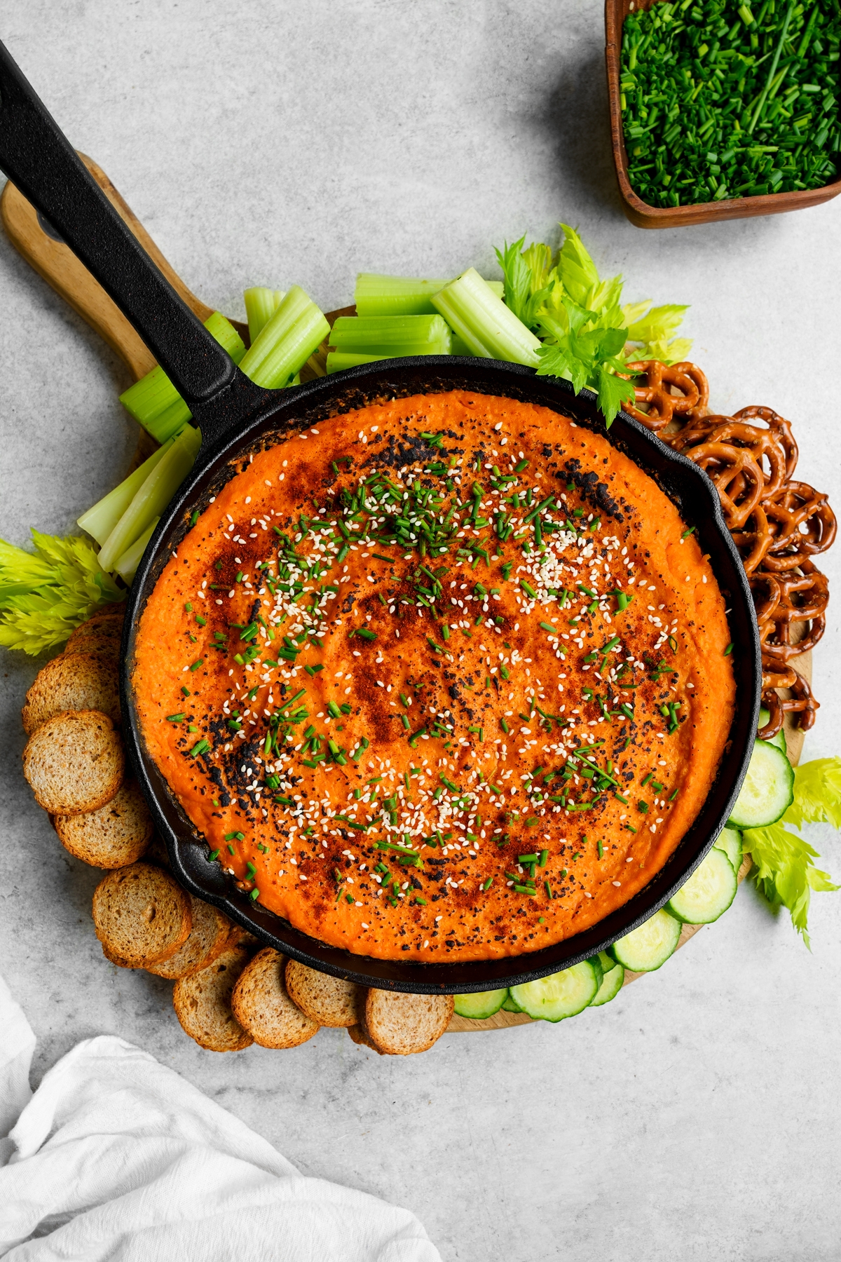 the vegan butternut squash dip in a cast iron skillet with celery, pretzels, cucumbers, and crackers around it