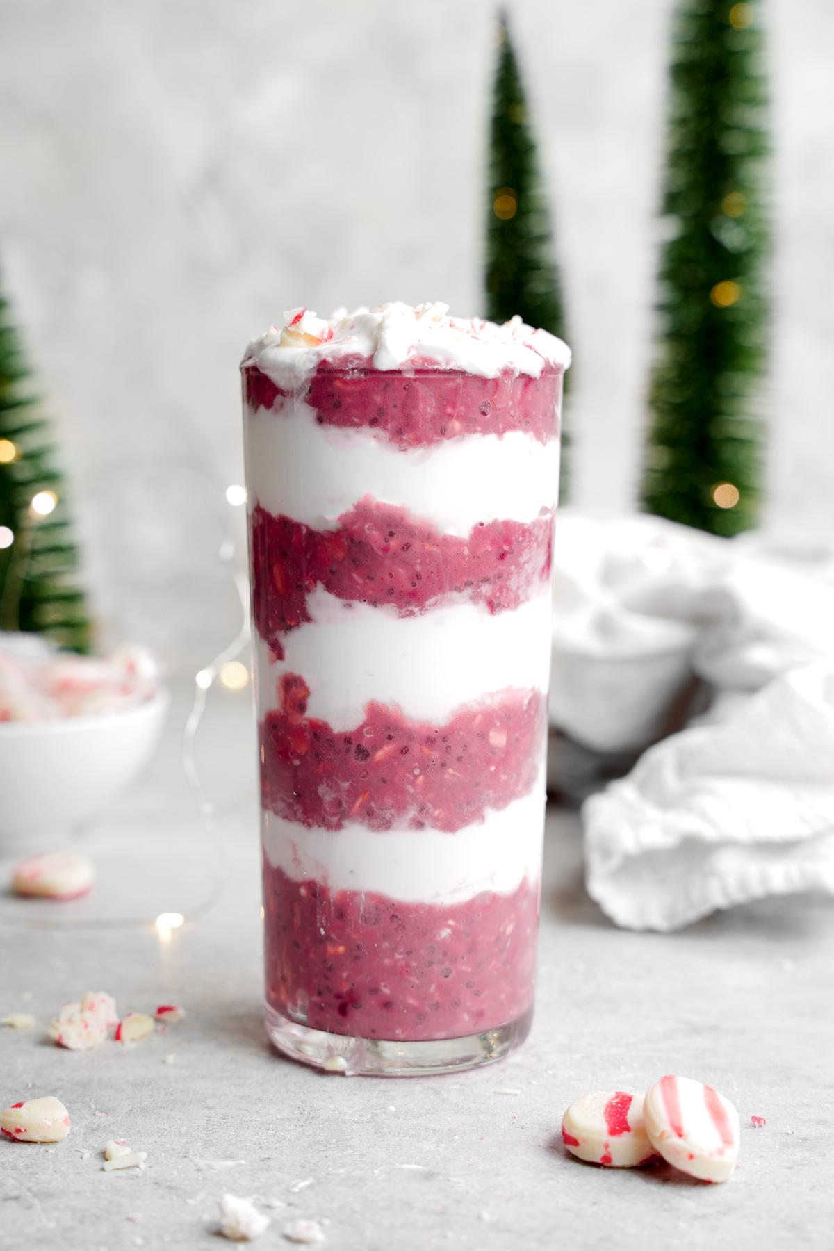 the peppermint overnight oats in a glass jar layered like a candy cane with christmas trees around it