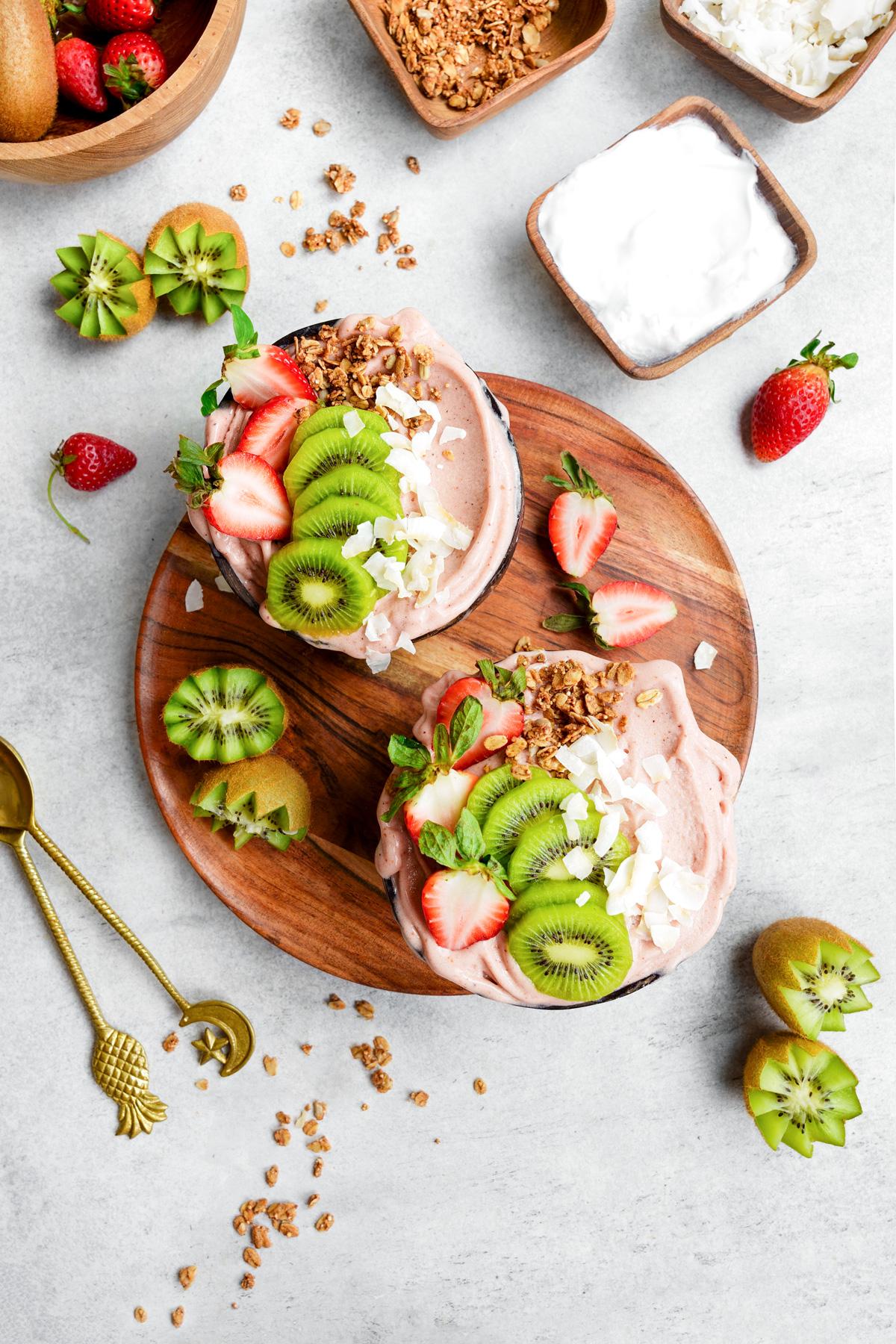 the strawberry smoothie bowls in coconut bowls with fresh strawberries and kiwis on top