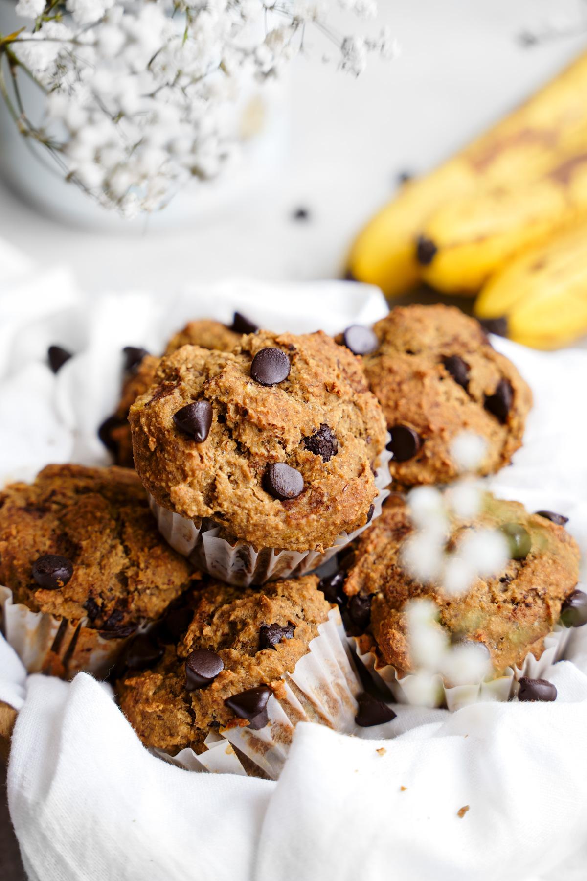 the banana chocolate chip protein muffins in a basket with fresh bananas and plantfusion protein in the back