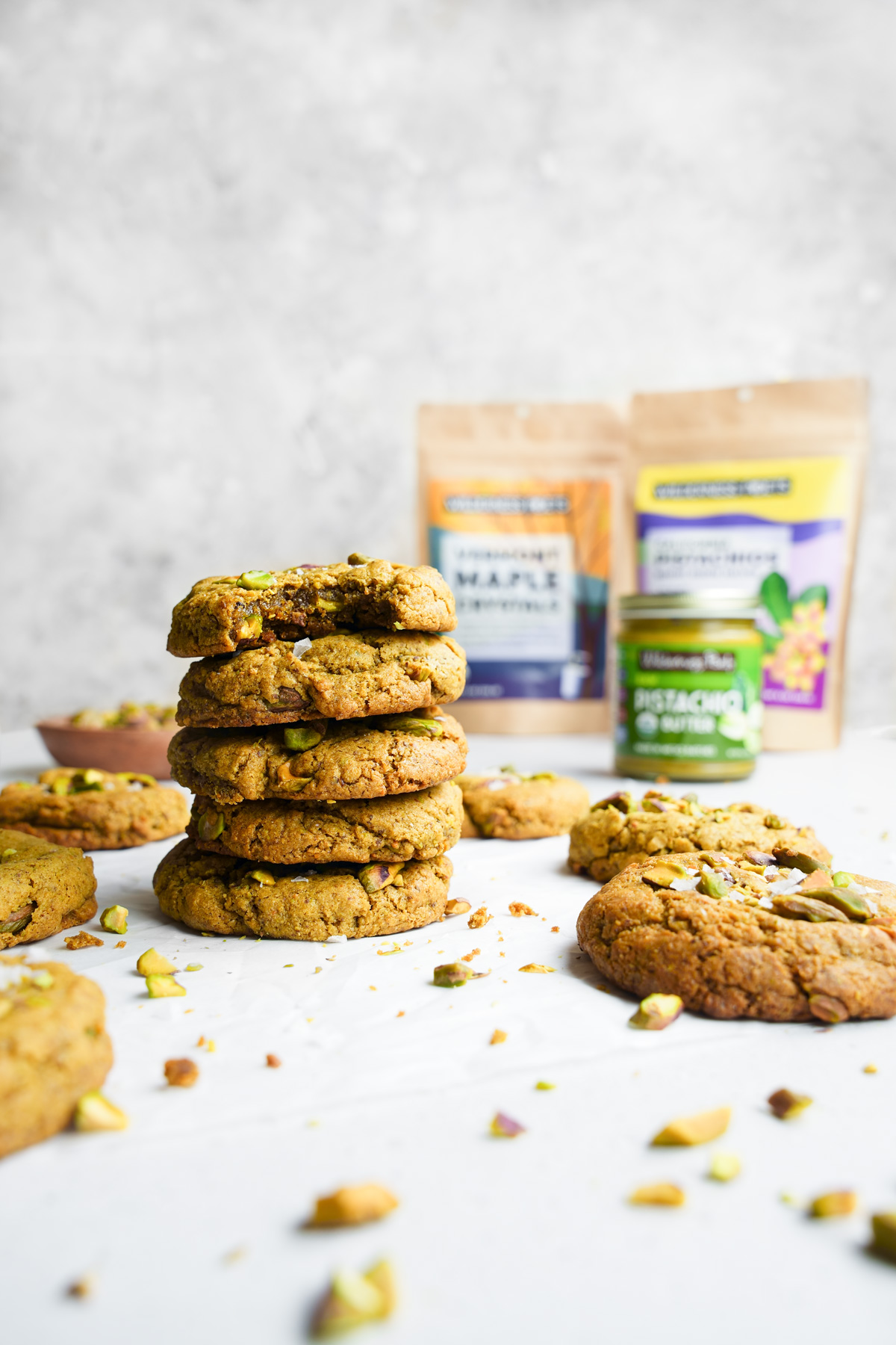 the vegan pistachio cookies stacked on top of each other with the wilderness poets products in the background