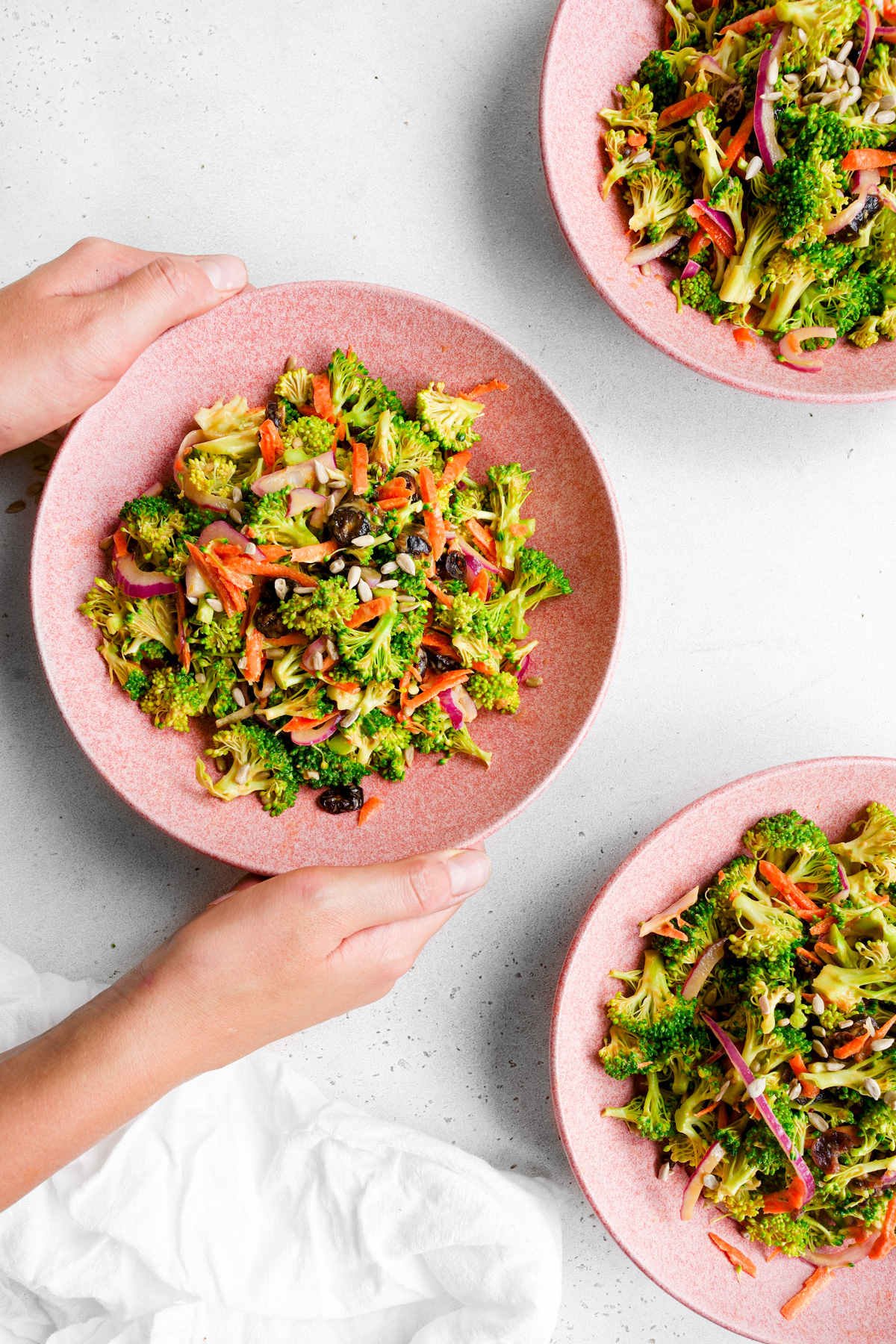hands holding the broccoli crunch salad in serving bowls 