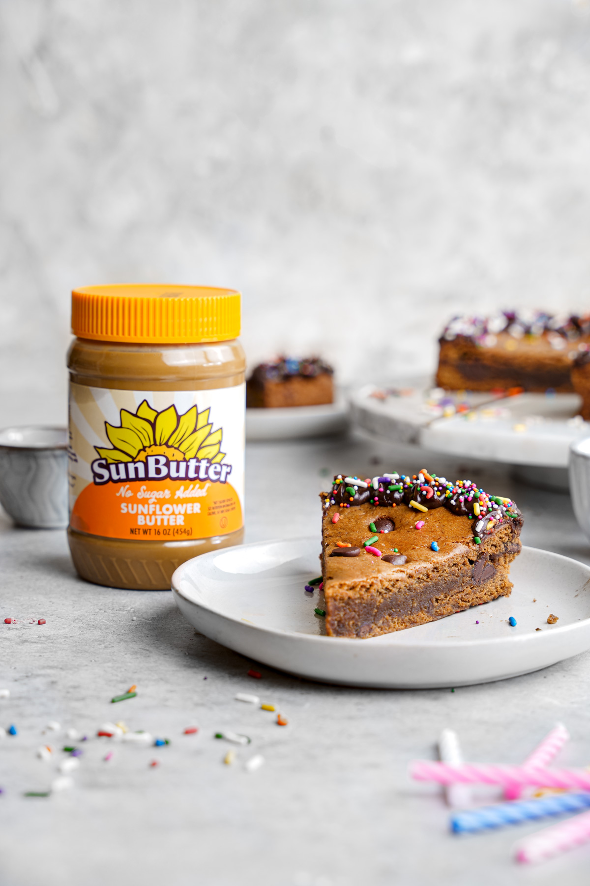 a slice of the cookie cake next to the sunbutter no sugar added sunflower butter
