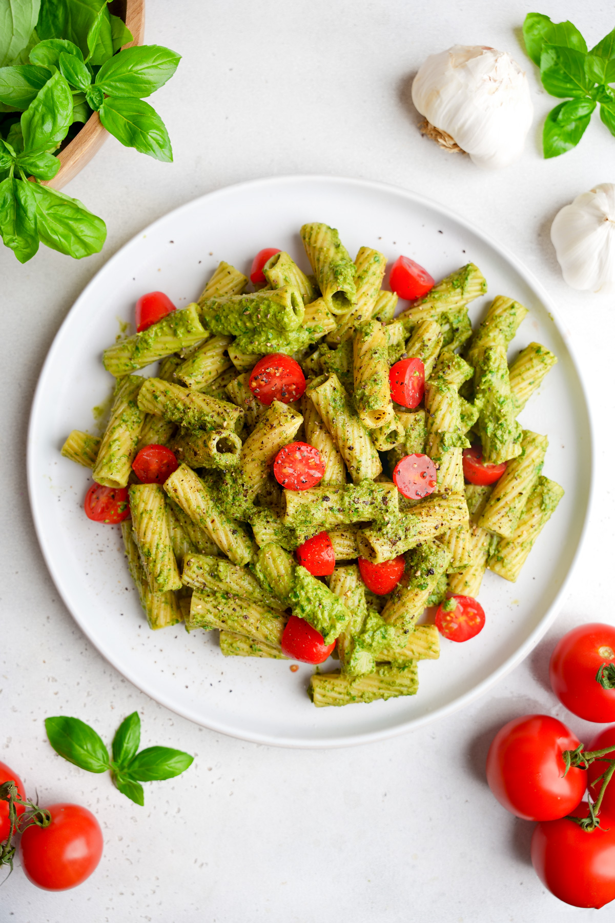 looking down at the nut free pesto pasta on a plate with fresh tomatoes and basil around