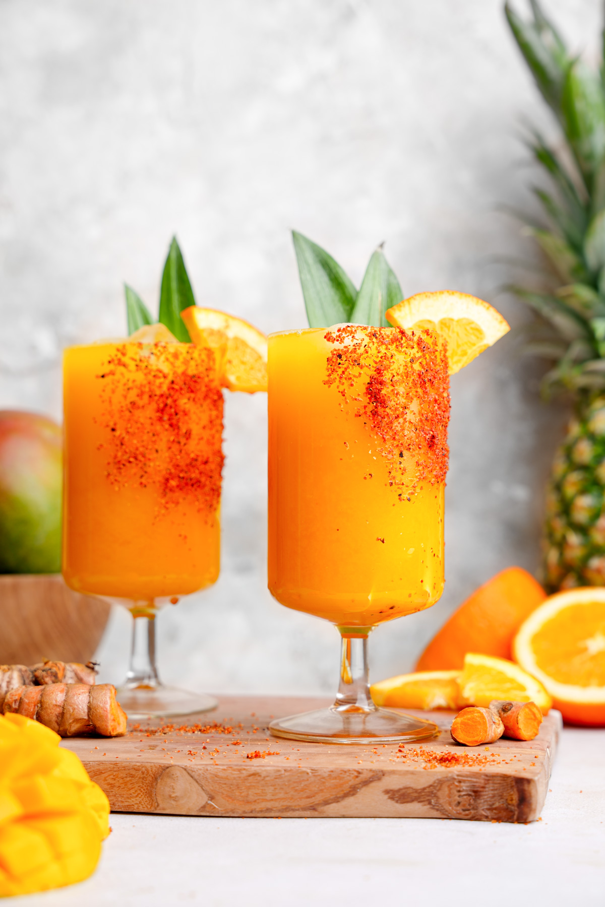 two glasses of the golden mango juice garnished with tajin oranges and pineapple leaves