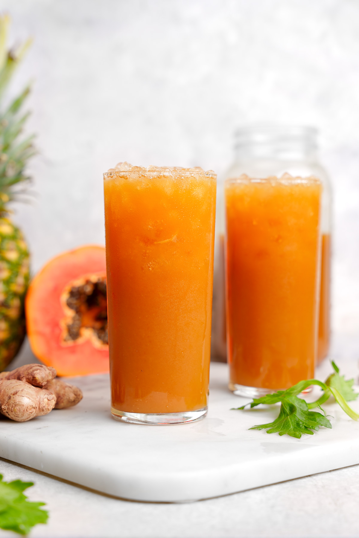 the two glasses of papaya juice with fresh ingredients all around