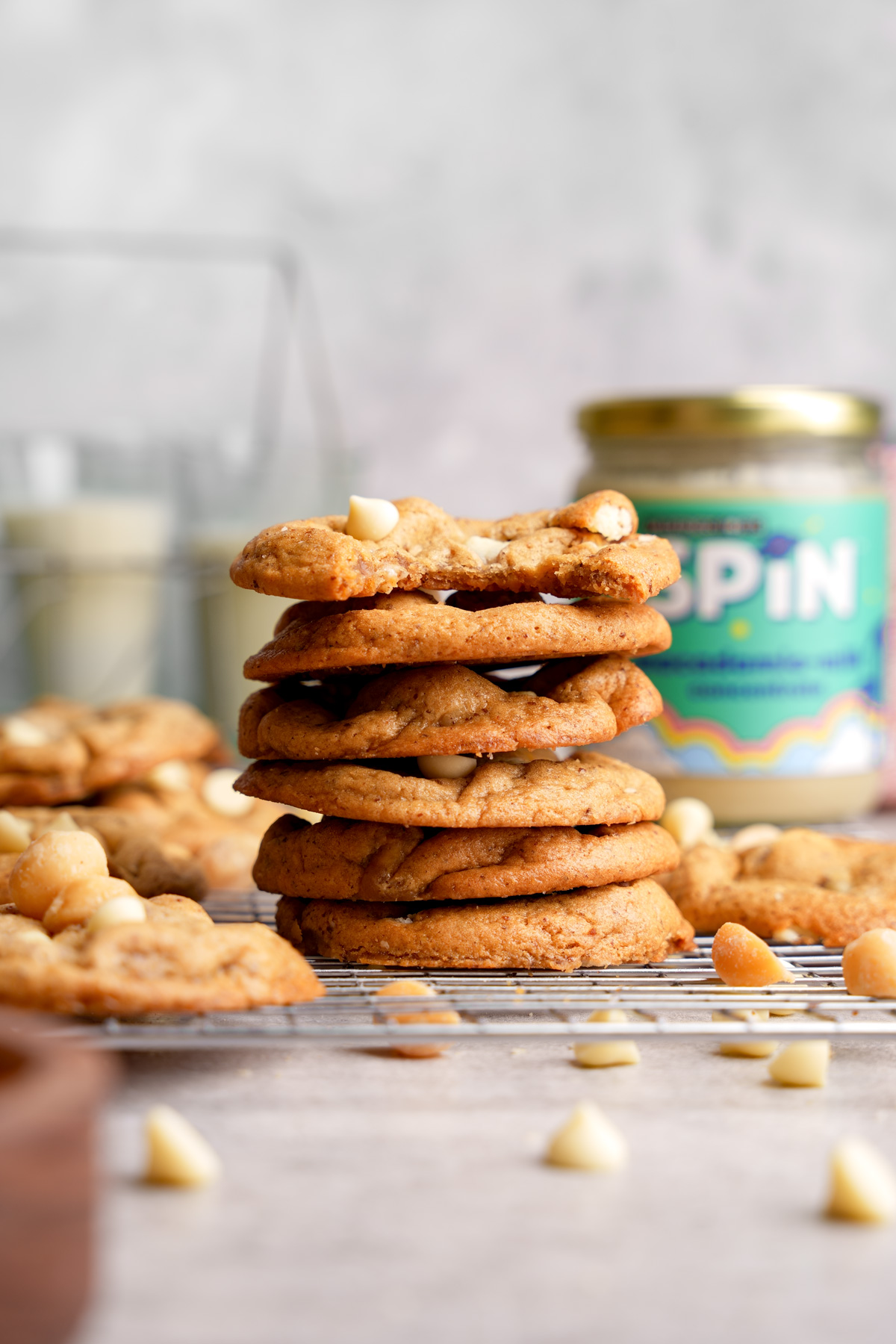 the vegan white chocolate macadamia nut cookies stacked on top of each other with the spin nut milk concentrate in the back