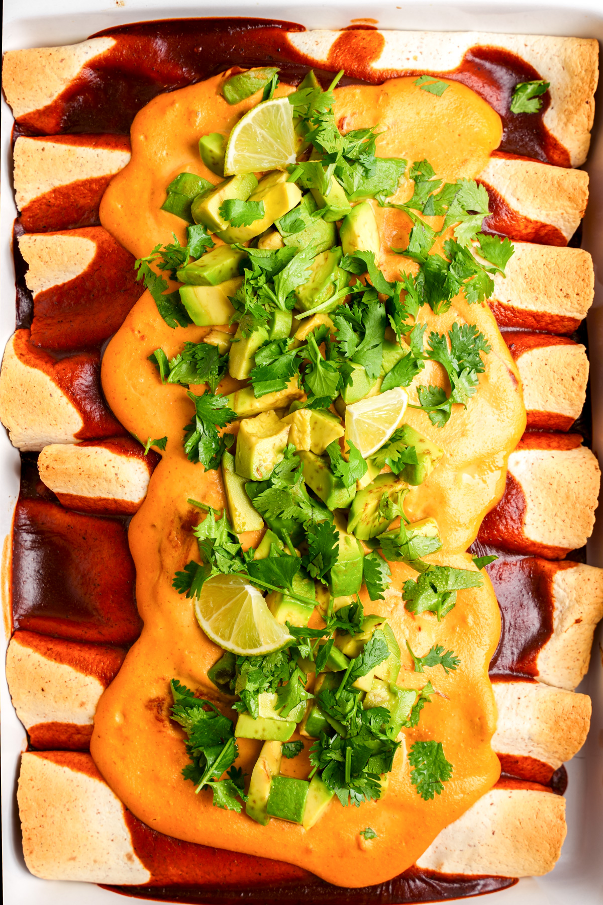 the enchiladas in a baking dish with the vegan nacho cheese sauce on top and fresh toppings