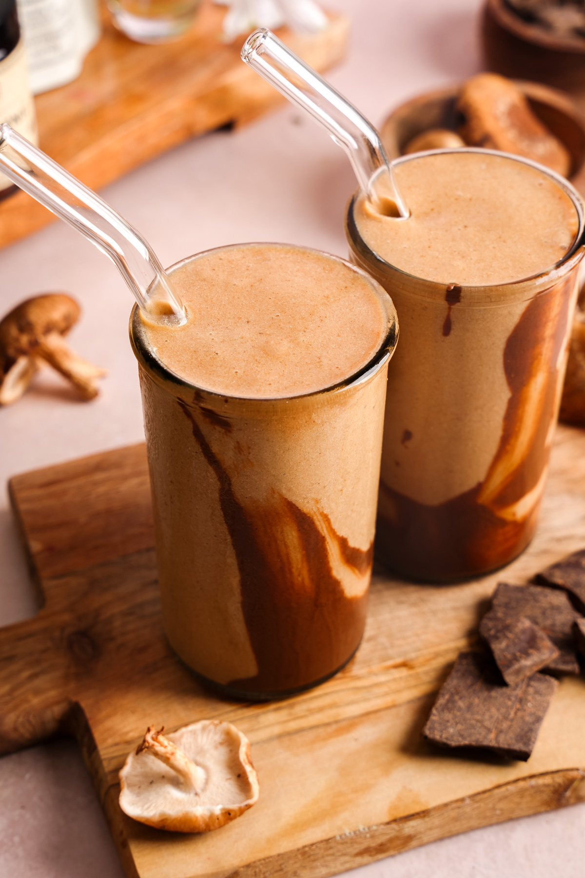 the adaptogenic mushroom smoothie in two tall glasses with chocolate and mushrooms around them