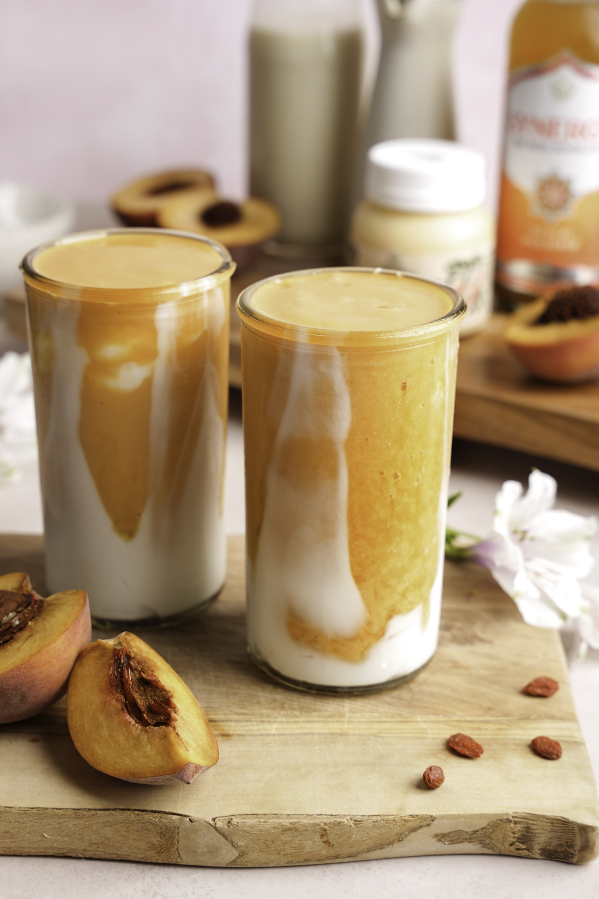 Homemade peaches and cream smoothie inspired by Kendall Jenner, swirled with creamy coconut yogurt and peach smoothie in tall glasses, styled with fresh peach slices, goji berries, and superfood ingredients on a wooden board.